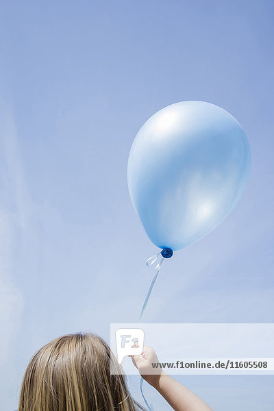 Kaukasisches Mädchen hält blauen Luftballon in blauem Himmel