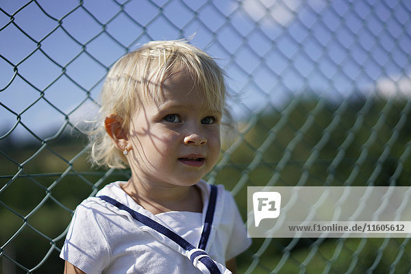 Cute toddler standing against chainlink fence