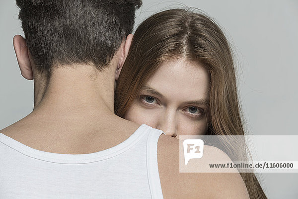 Portrait of woman with long brown hair embracing boyfriend against gray background