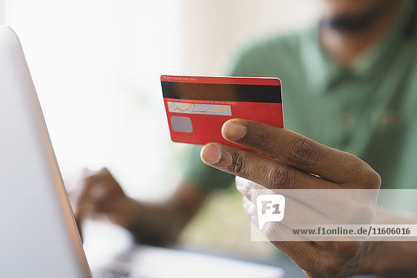 Abgeschnittenes Bild des Mannes  der beim Online-Shopping über den Laptop zu Hause Kredit hält