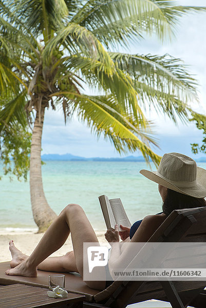Frau liest Buch am tropischen Strand
