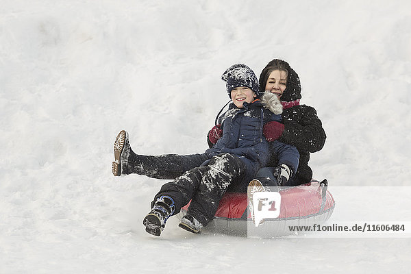 Porträt einer glücklichen Großmutter und eines Enkels auf einem aufblasbaren Ring im Schnee.