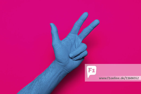 Nahaufnahme der blau bemalten Hand mit Friedenszeichen auf rosa Hintergrund