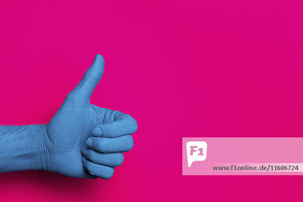 Nahaufnahme der blau bemalten Hand mit Daumen vor rosa Hintergrund