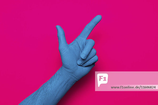 Nahaufnahme einer blau bemalten Hand  die auf rosa Hintergrund zeigt.