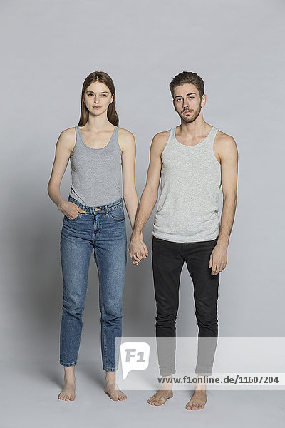Portrait of couple holding hands while standing against gray background