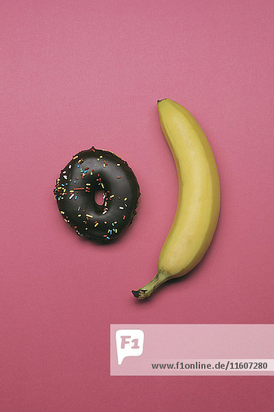 Direkt über Schuss Donut und Banane auf rosa Hintergrund