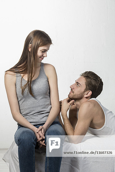Smiling man looking at girlfriend while resting on sofa against white background