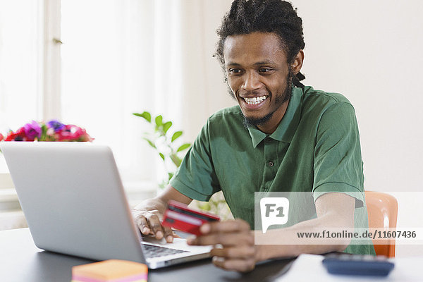 Glücklicher Mann online einkaufen durch Laptop zu Hause