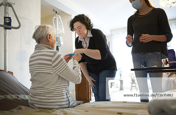 Reportage über einen häuslichen Pflegedienst in Savoie  Frankreich. Eine Hilfskrankenschwester gibt einem Patienten eine Tablettenschachtel.