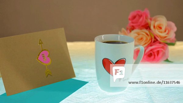 Dampfende Kaffeetasse mit Herz  Blumen und Karte auf dem Tisch