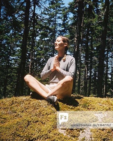 Frau in Yoga-Pose auf moosigem Boden