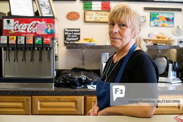 Harrison  New York  USA. Female lunch room owner leaning on the counter of her store  just after lunch time.
