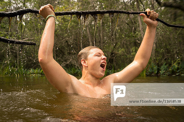 Teenager Junge im Wasser  der jubelnd einen Baumzweig hält  Turkey Creek  Niceville  Florida  USA