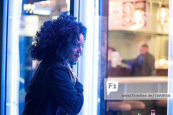 Frau  die nachts durch das Fenster eines Cafés schaut