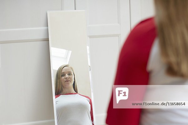 Junge Frau betrachtet ihr Spiegelbild.