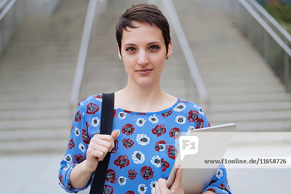 Porträt einer mittleren erwachsenen Frau  die im Freien steht und Tasche und Laptop hält