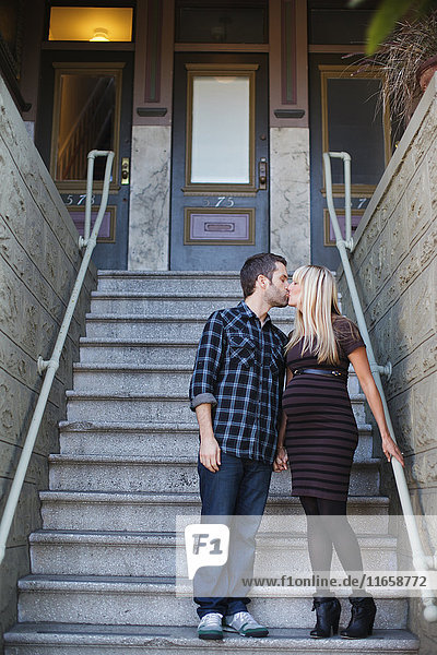 Pregnant mid adult woman kissing boyfriend outside house stairway