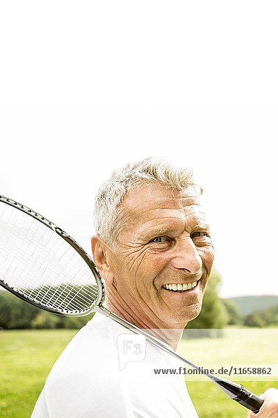Älterer Mann mit Badmintonschläger  lächelnd.