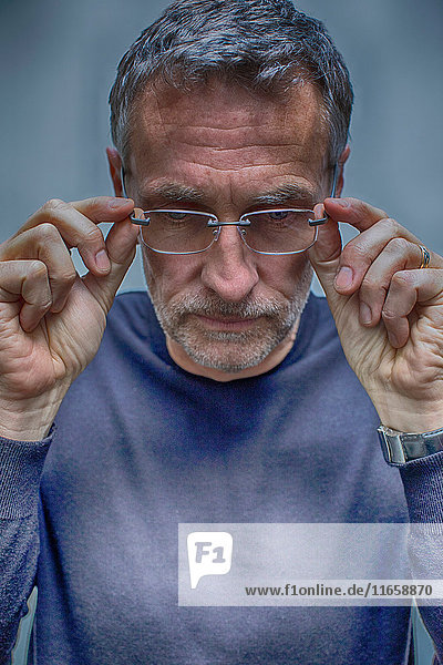 Porträt eines ergrauten reifen Mannes beim Abnehmen der Brille