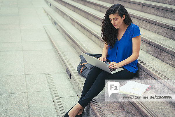 Junge Frau sitzt auf Stufen und benutzt Laptop