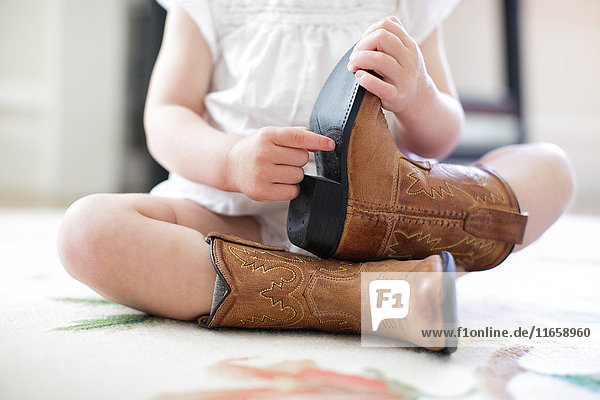 Neck down view of female toddler sitting on floor wearing cowboy boots