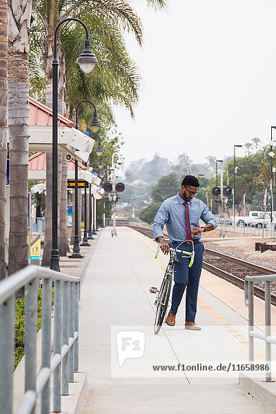 Junger Geschäftsmann Radfahrer schaut auf dem Bahnsteig des Bahnhofs auf die Uhr