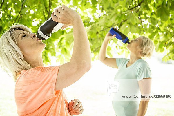 Zwei Frauen trinken Wasser aus Sportflaschen.