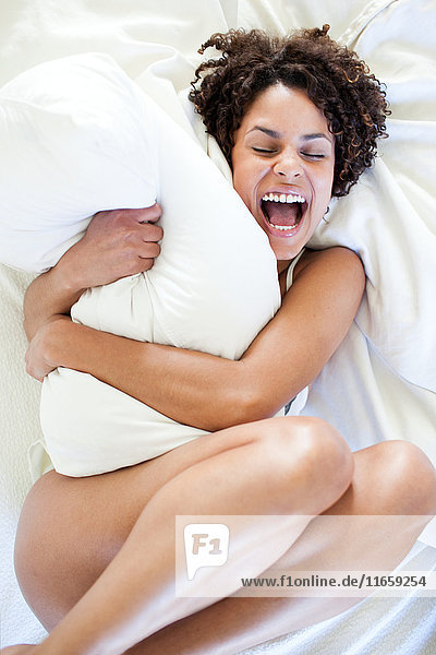 Draufsicht einer nackten Frau  die auf einem Bett liegt und ein Kissen umarmt