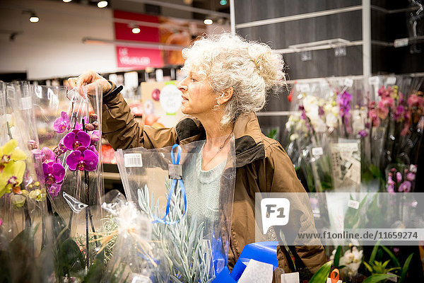 Reife Frau im Supermarkt,  die sich Pflanzen und Blumen ansieht