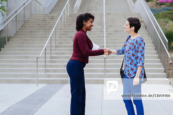 Zwei Frauen stehen im Freien  schütteln Hände und lächeln