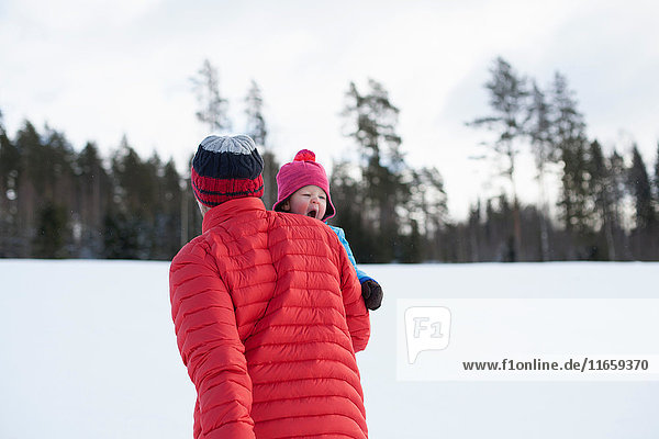 Vater trägt kleinen Sohn in schneebedeckter Landschaft