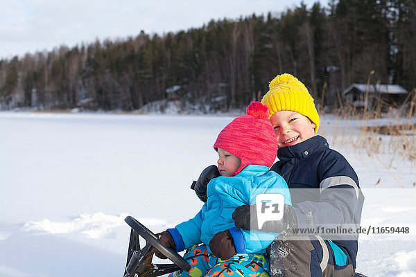 Two young brothers sitting on sledge  in snow covered landscape