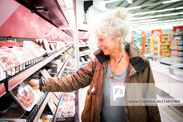Reife Frau im Supermarkt mit Blick auf die Kühlfleischabteilung