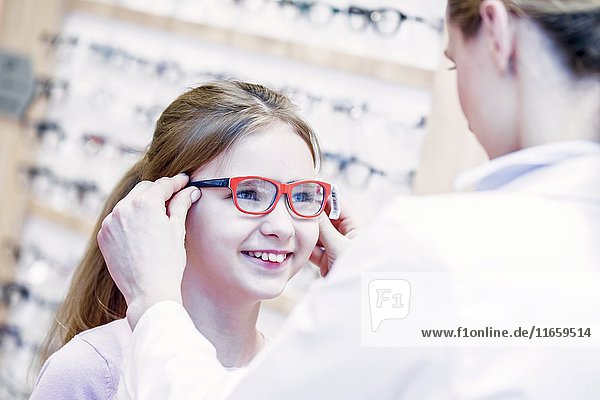 Optiker probiert eine Brille für ein Mädchen in einem Optikerladen an.