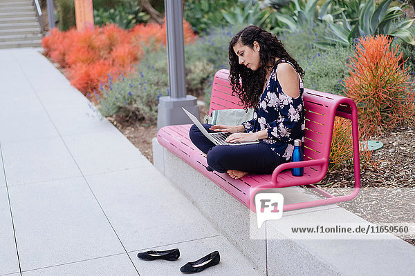 Junge Frau sitzt auf Bank und benutzt Laptop
