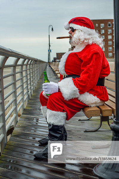 Mann im Weihnachtsmannkostüm  auf Bank sitzend  Zigarre rauchend  Bierflasche haltend