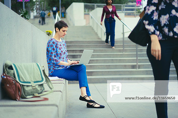 Junge Frau sitzt im Freien und benutzt einen Laptop