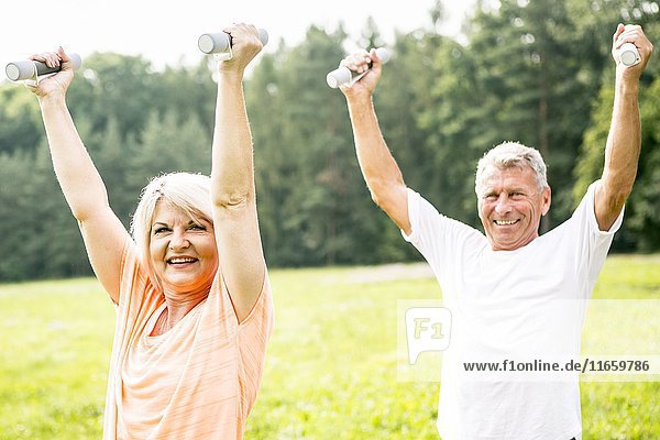 Älteres Paar trainiert mit Handgewichten auf einem Feld.