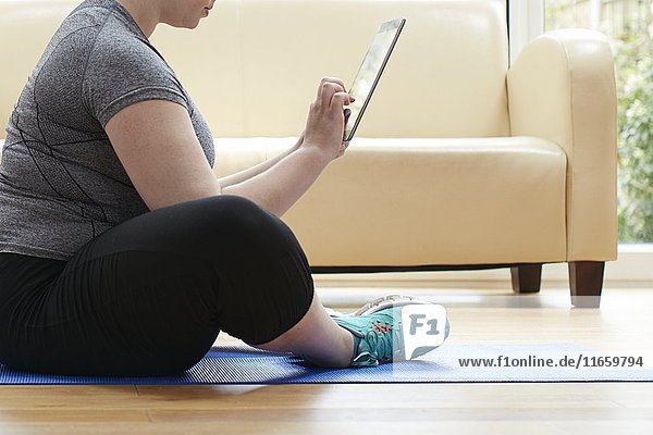Frau sitzt auf dem Boden und benutzt ein digitales Tablet.