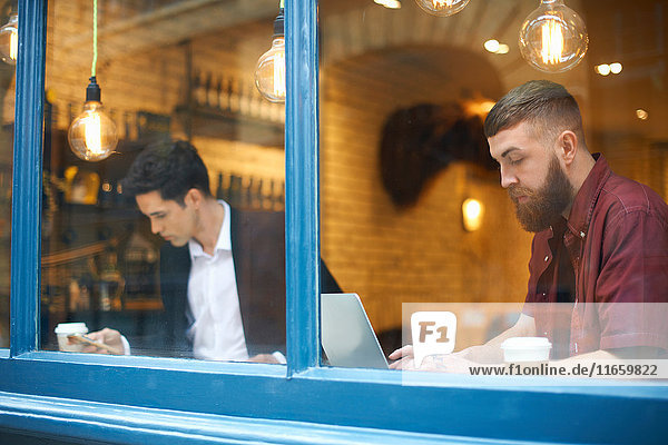 Fensteransicht von Geschäftsleuten mit Laptop und Blick auf das Smartphone im Cafe