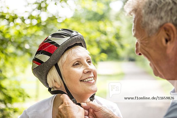 Mature woman wearing bicycle helmet  senior man assisting.