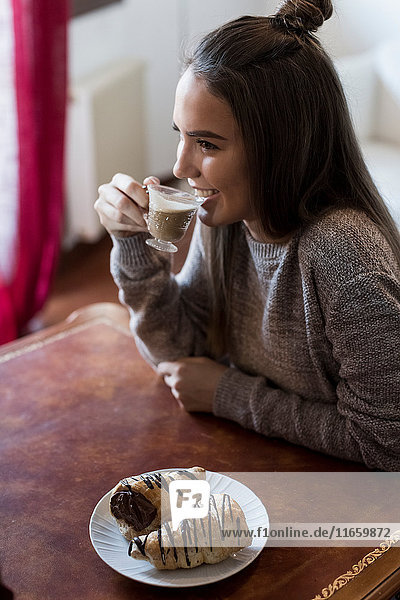 Young woman sitting at table drinking coffee pastry on table in front of her