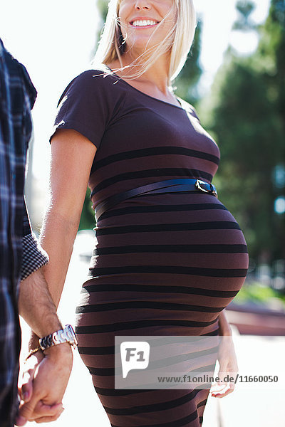 Cropped shot of pregnant mid adult woman holding hands with boyfriend