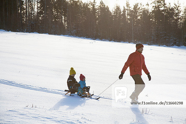 Vater zieht Söhne auf Schlitten in schneebedeckter Landschaft mit