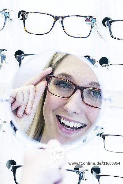 Woman trying on glasses in optometrist's shop in front of mirror.
