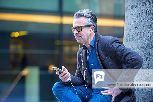Mann mit Smartphone und Ohrstöpseln im Freien