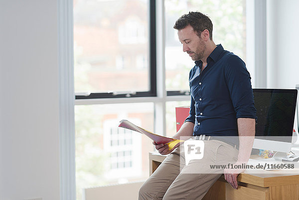 Man contemplating and reading papers by office window
