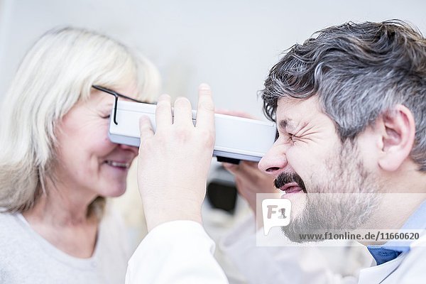 Optometrist  der einen Sehtest bei einer älteren Frau mit Sehtestgerät in einem Optometristengeschäft durchführt.