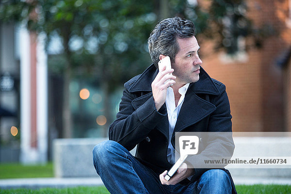 Mann beim Telefonieren mit dem Smartphone im Freien sitzend